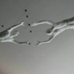 Two white sculptures of people reaching for each other