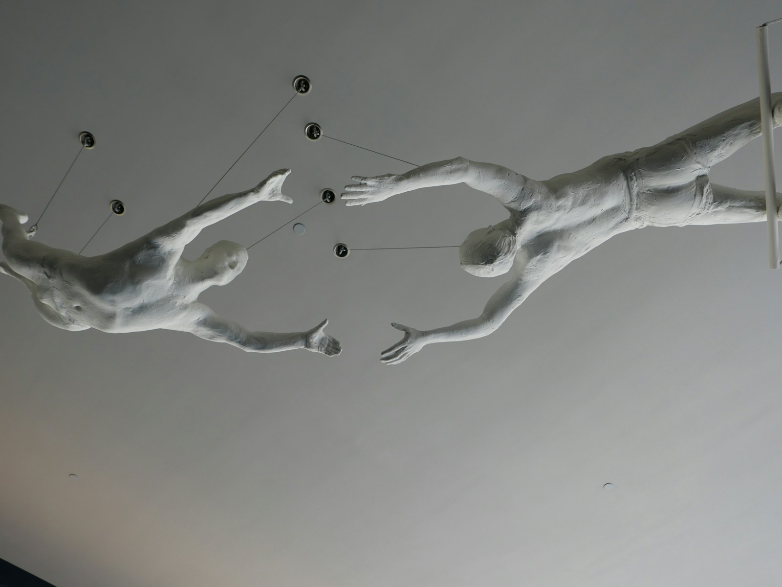 Two white sculptures of people reaching for each other